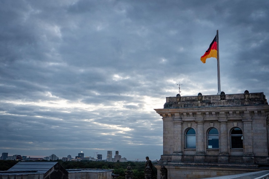 A building with a German flag on it. Other large buildings are visible in the distance.