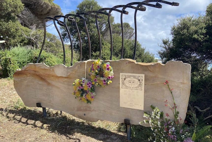 A wooden monumnet with bushland behind it and fresh flower wreaths hung up on it.