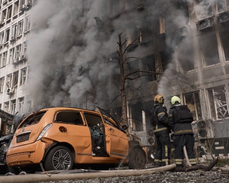 Firefighters in Kyiv work before a smoking building beside a wrecked car after a drone strike