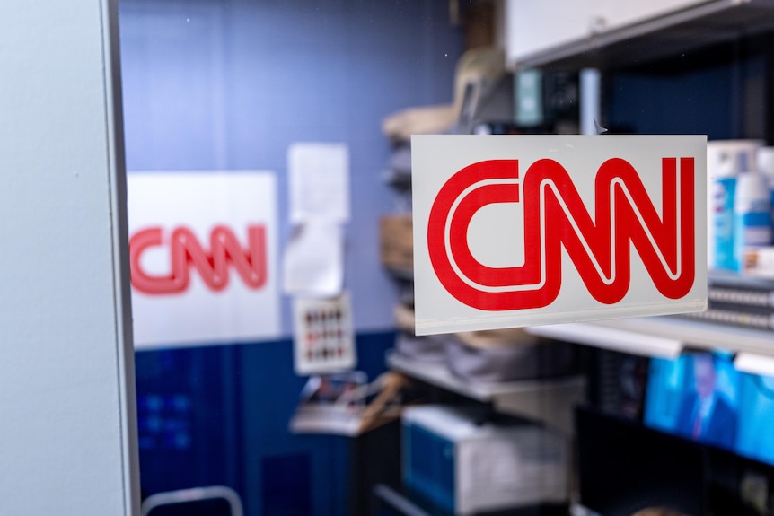 A sign with the CNN logo posted on a glass wall, with a desk behind it.