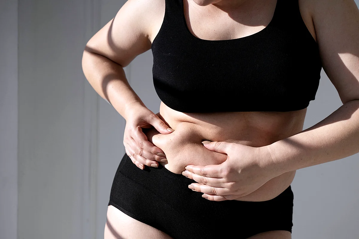 mulher mede gordura abdominal, conhecida como pochete, com as mãos