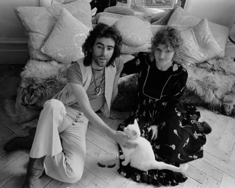 Ossie Clark and Celia Birtwell sit on a cushioned floor, he petting a white cat