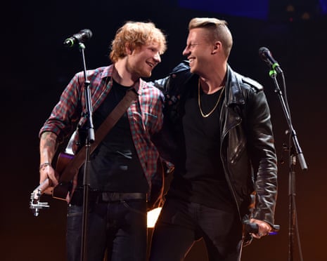 Ed Sheeran and Macklemore smile at each other on stage during a concert performance