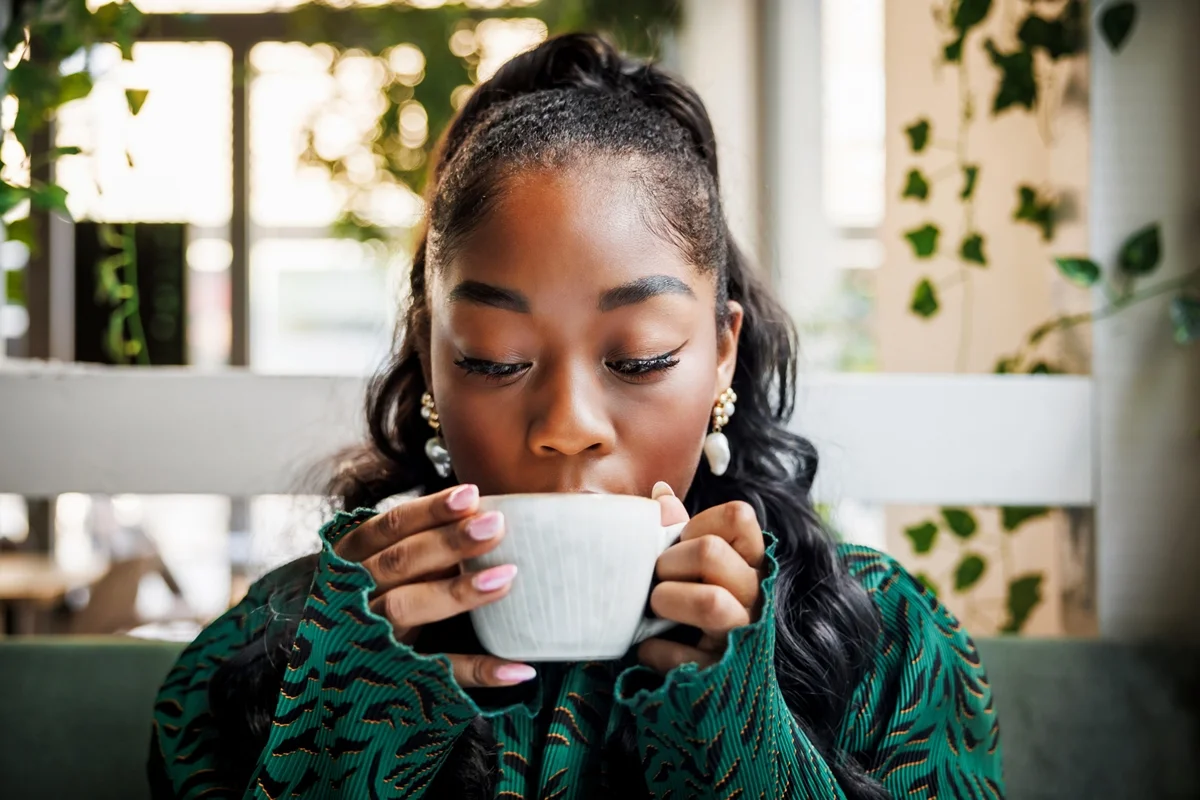 Uma jovem se delicia com o aroma do seu café, fechando os olhos para saborear o momento em um ambiente arborizado de cafeteria. bebida Caneca xíacara café chá