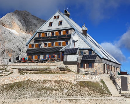 A mountain hut with a rock mountain peak visible in the background