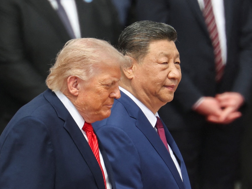 Trump and Xi walk past a group of people standing on steps.