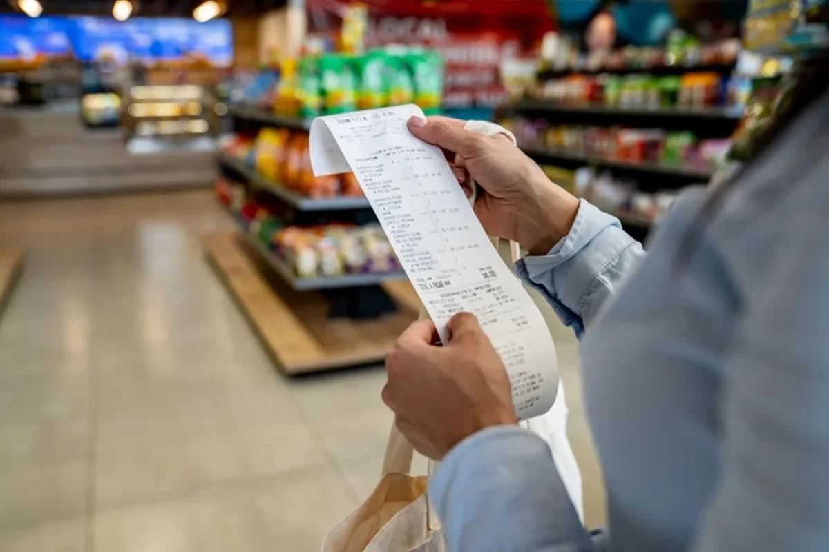 Imagem colorida de consumidor com cupom fiscal no supermercado
