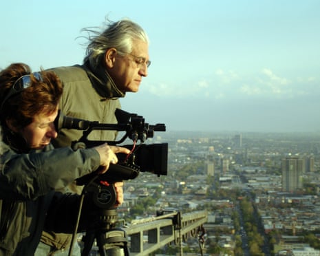 Director Patricio Guzman and a colleague film with a camera on a tripod overlooking a sprawling city