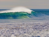 A nice image of a wave curling over towards the shore. The water is lush green and blue.