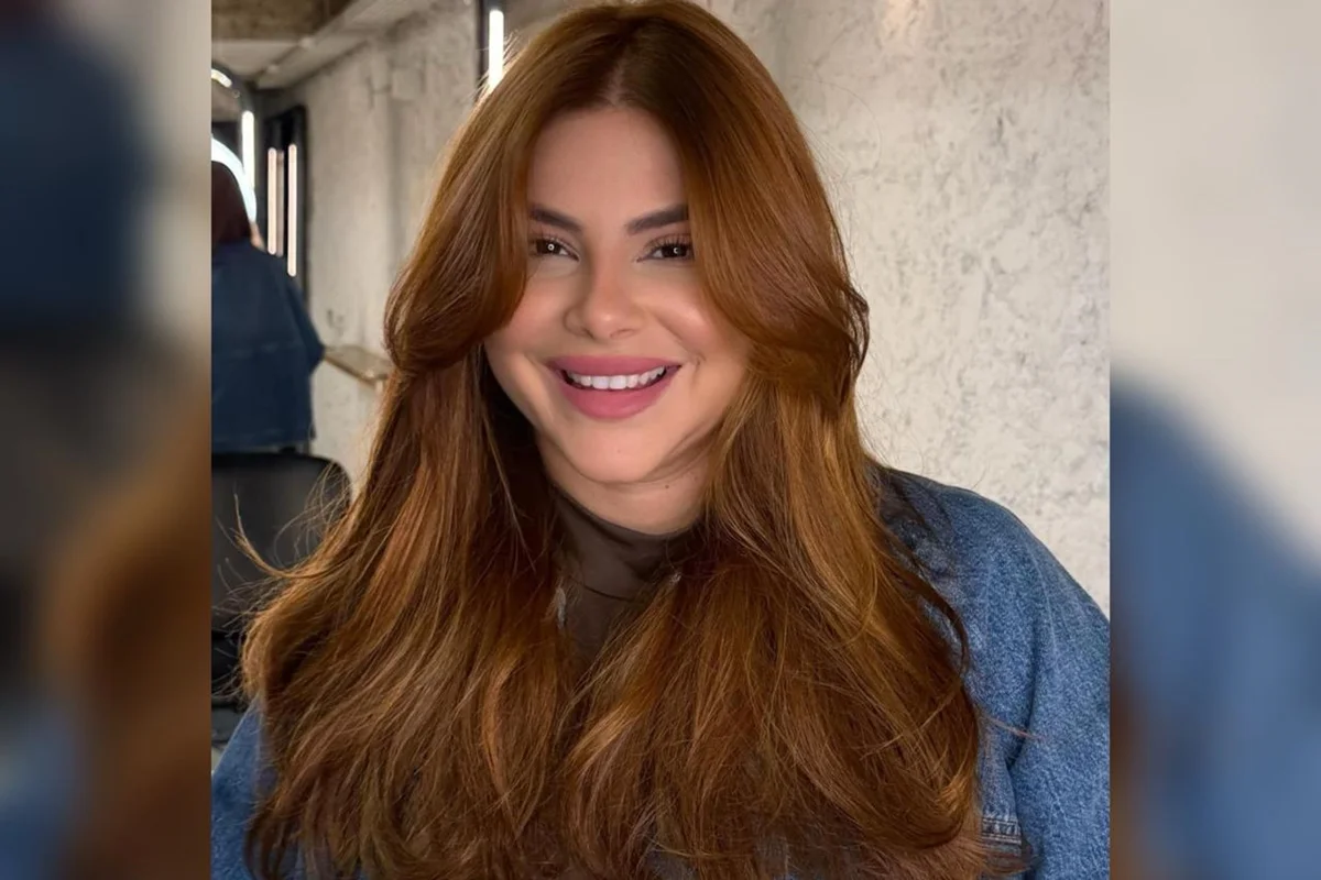 foto clorida de mulher com cabelos ruivos e jaqueta jeans, sorrindo para foto - Metrópoles.