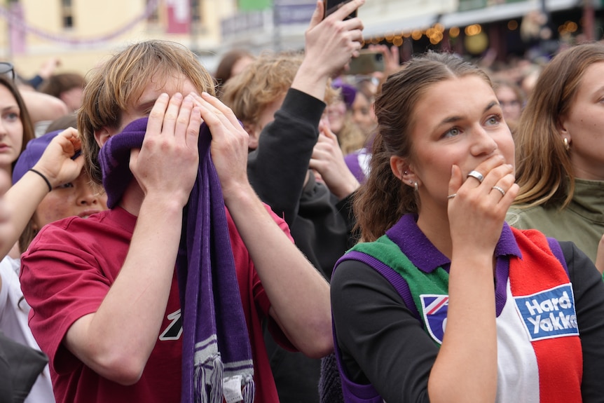 Fremantle fans wearing club merchandise hold their heads in their hands