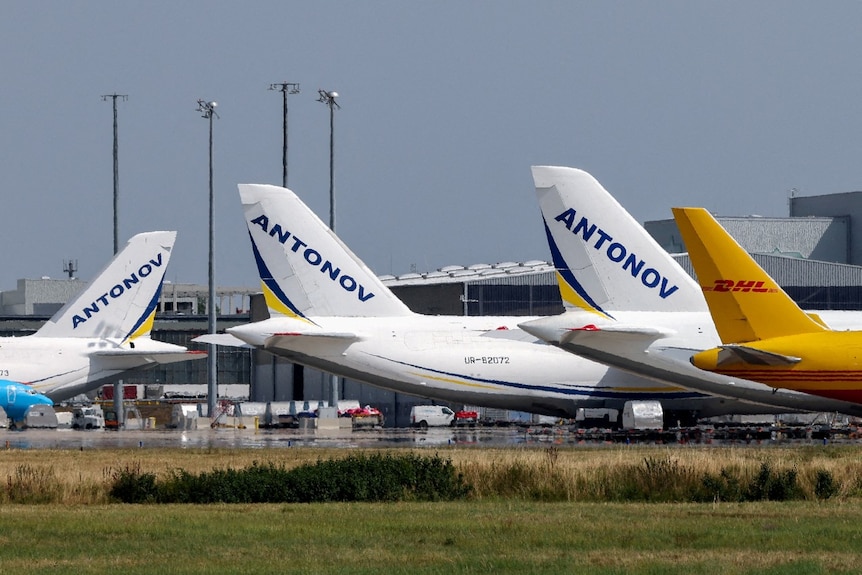 Several aircraft lined up at a terminal. Some have the word Antonov written on their tails.