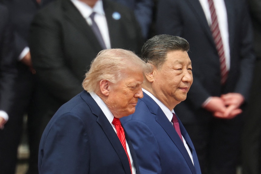 Trump and Xi walk past a group of people standing on steps.