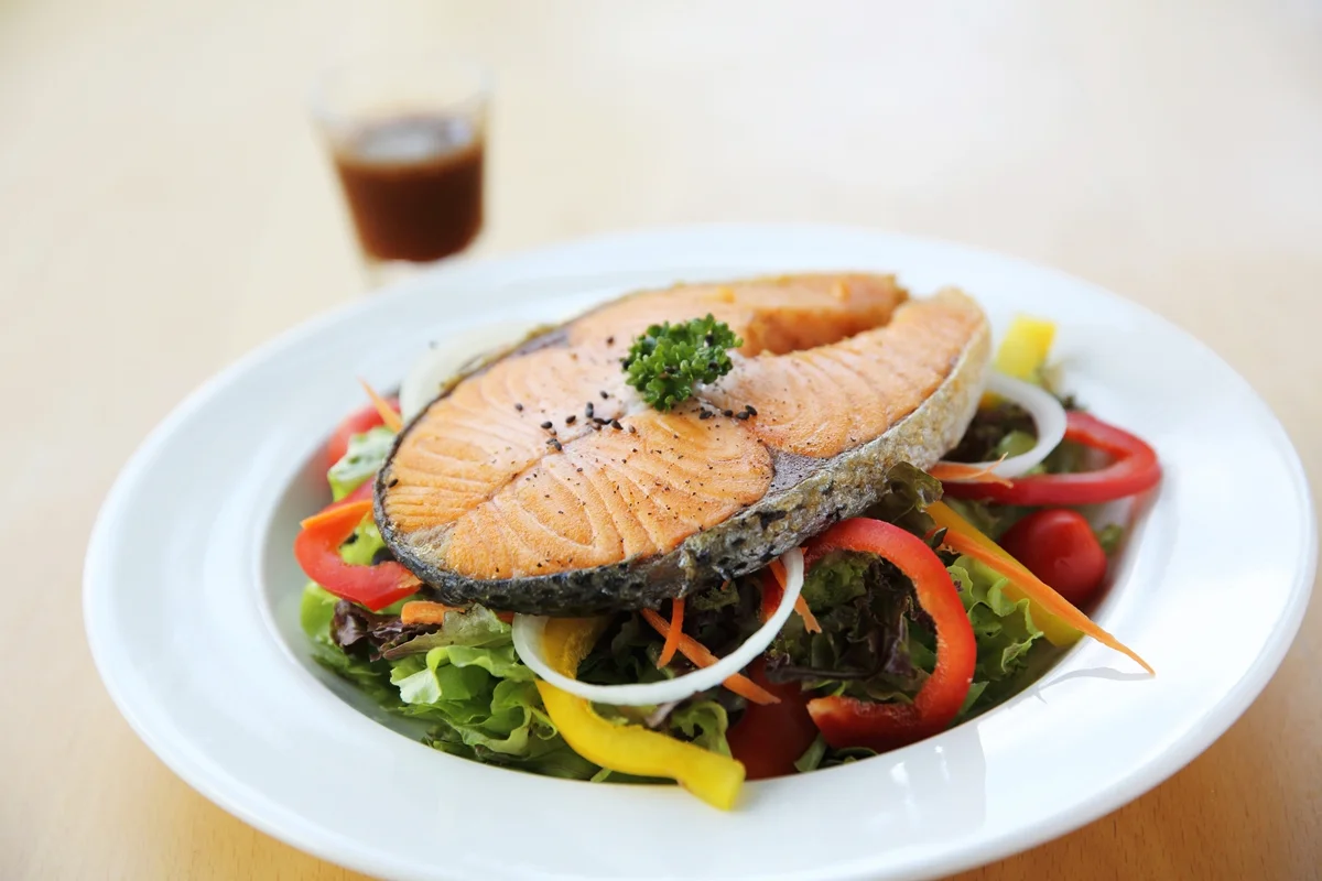 Foto colorida de peixe e salada em prato branco - Metrópoles