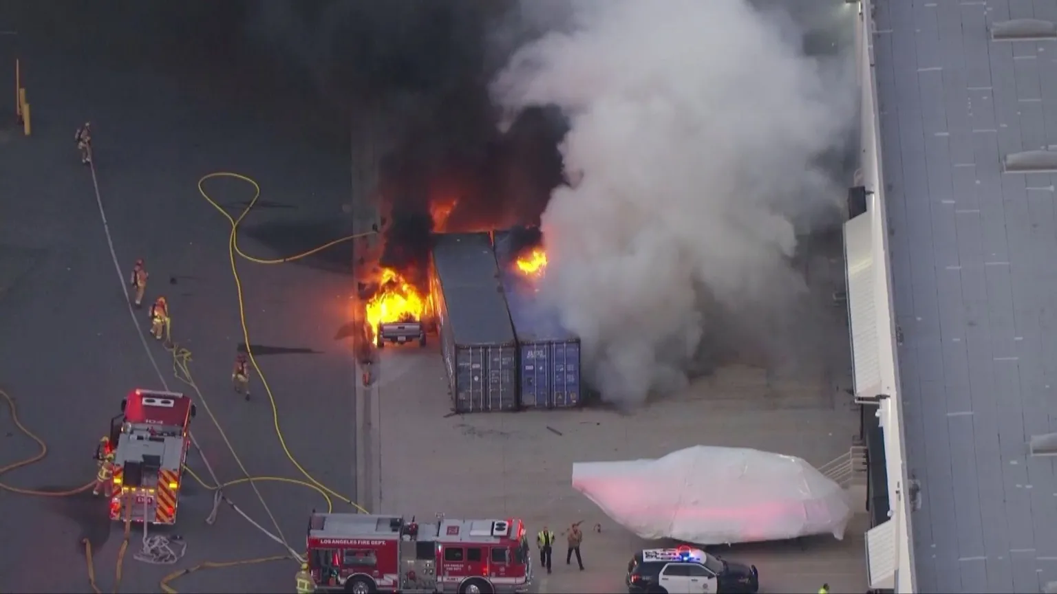 CBS A vehicle appears to be on fire next to shipping containers. Smoke is billowing from the containers.