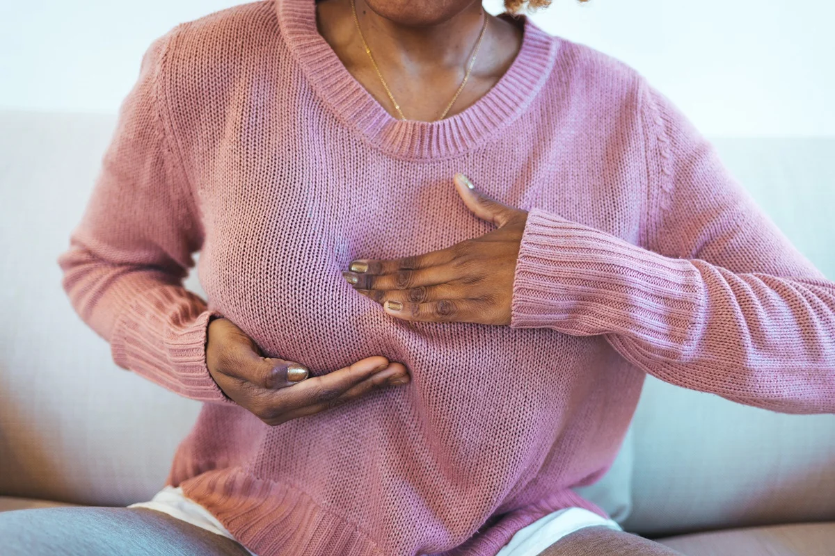 Foto colorida de mulher negra segurando os seios - Desigualdade afeta tratamento de câncer de mama em mulheres negras - Metrópoles