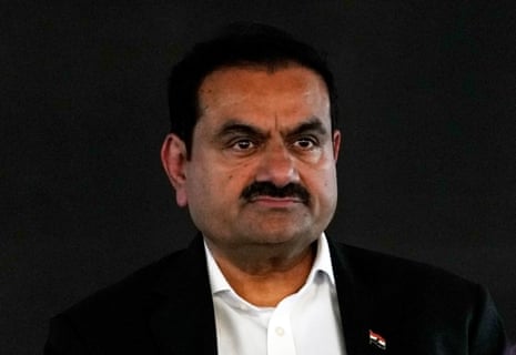 Gautam Adani, in a dark suit, looks ahead against a black background