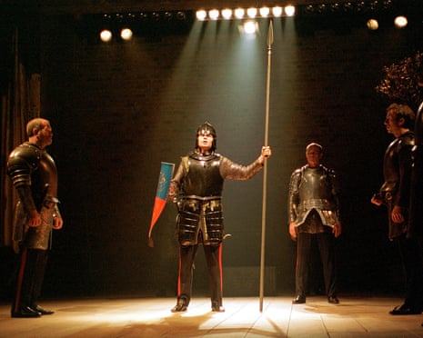 In Edward III, a knight raises a spear under a spotlight, watched by three armoured men