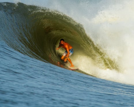 A surfer crouches on his board inside the barrel of a large curling wave in El Salvador