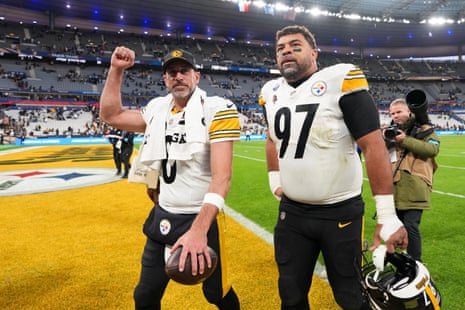 Aaron Rodgers and Cameron Heyward of the Steelers stand on the field, one raising his fist